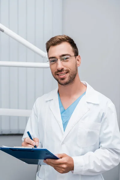 英俊的胡子医生在眼镜拿着剪贴板在诊所 — 图库照片