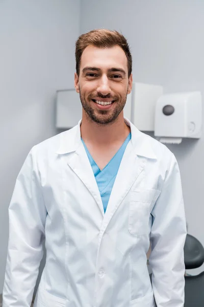 Szczęśliwy Brodaty Lekarz Białym Płaszczu Patrząc Kamerę Stojąc Klinice — Zdjęcie stockowe