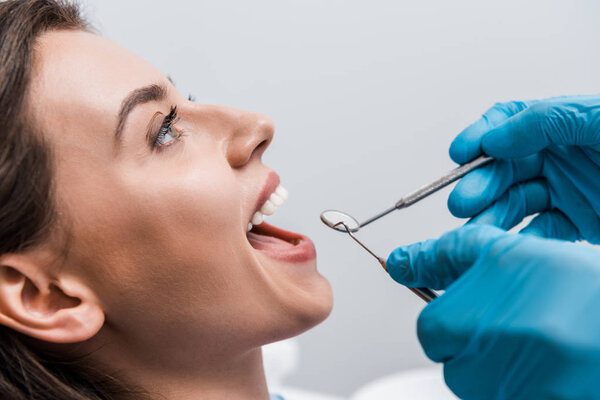 cropped view of dentist in latex gloves holding dental instruments near attractive woman 