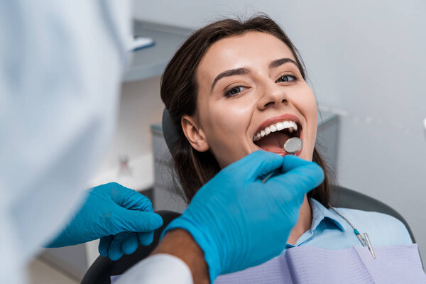 selective focus of dentist in latex gloves holding dental mirror near woman 