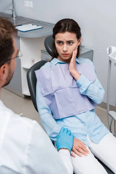 selective focus of upset woman touching face and looking at dentist