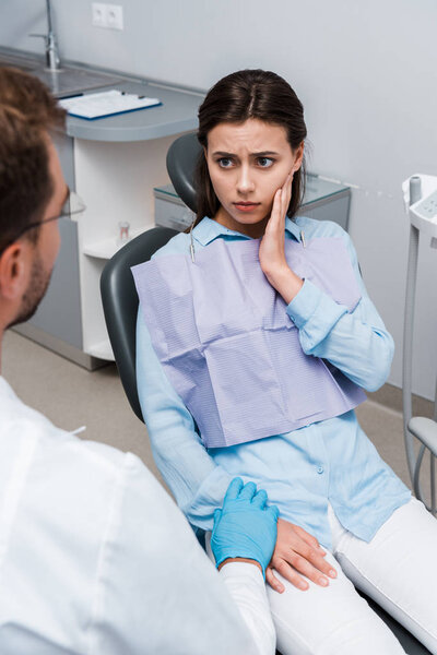 selective focus of upset woman touching face and looking at dentist 
