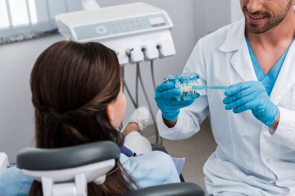 cropped view of dentist in latex gloves holding toothbrush near teeth model and girl 