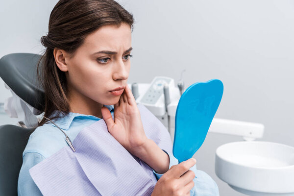 привлекательный и расстроенный девушка трогательное лицо при зубной боли и глядя на зеркало в клинике
 
