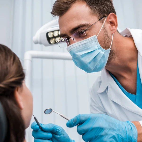 牙医在眼镜和医疗面罩中选择性的焦点 在患者附近持有牙科仪器 — 图库照片