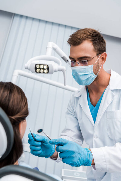 selective focus of dentist in glasses and medical mask holding dental instruments near woman 