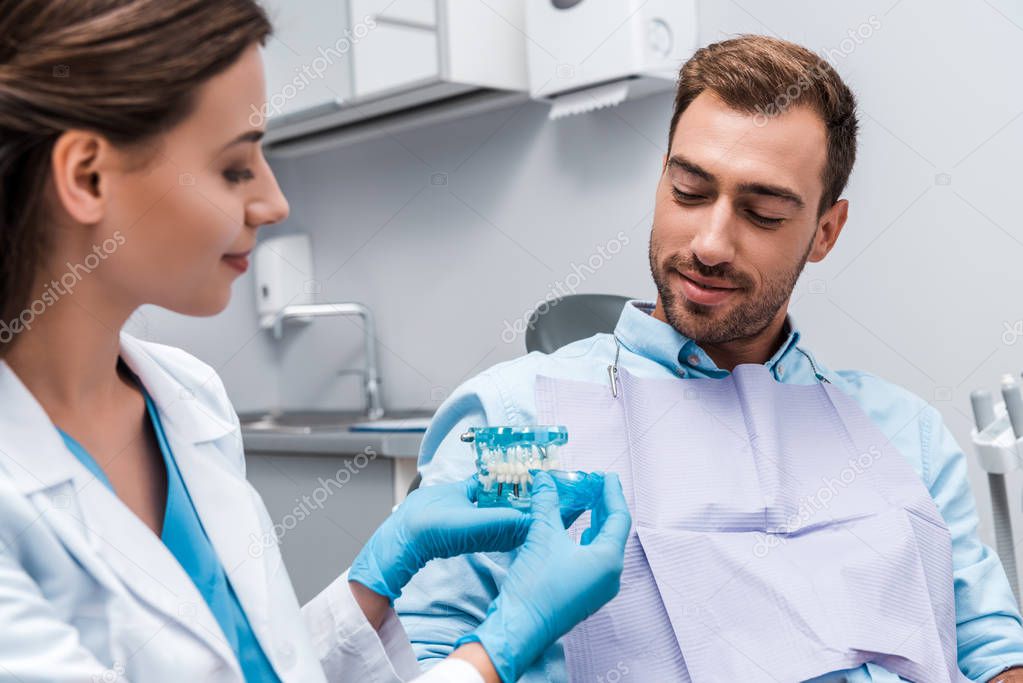 selective focus of man looking at teeth model in hands of attractive dentist 