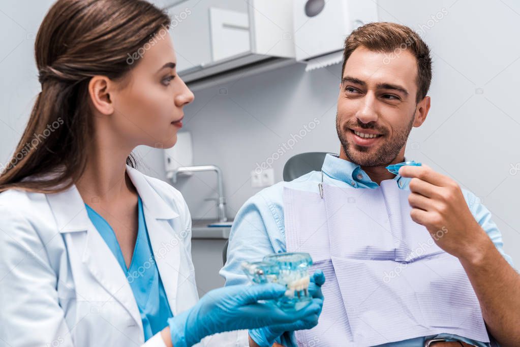 selective focus of handsome man holding retainer near dentist with teeth model in hands 