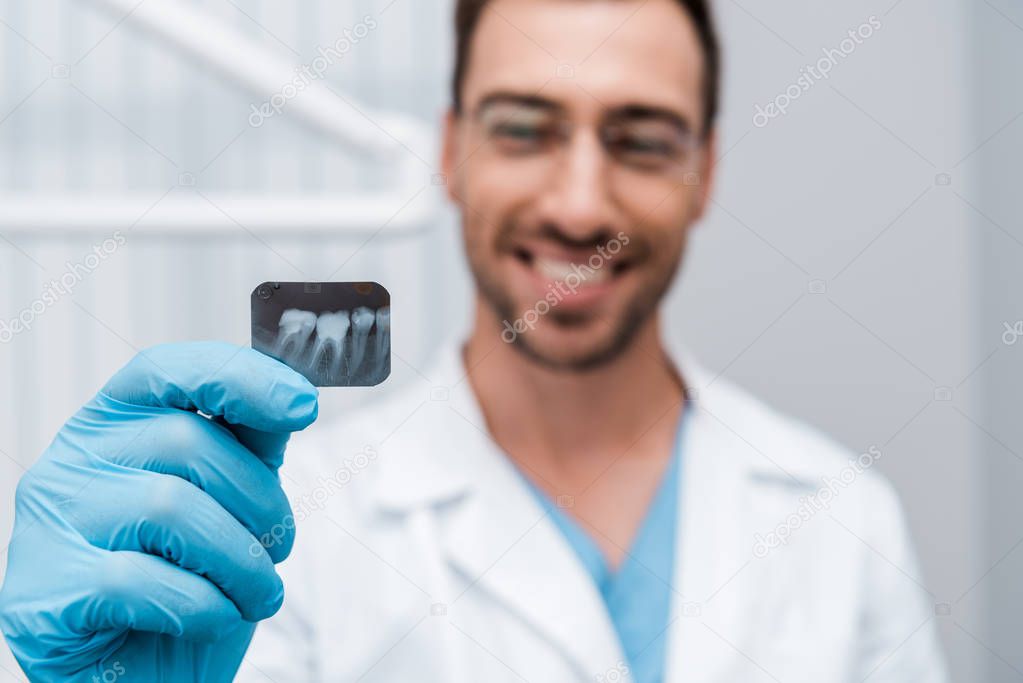 selective focus of x-ray in hand of cheerful dentist in dental clinic 