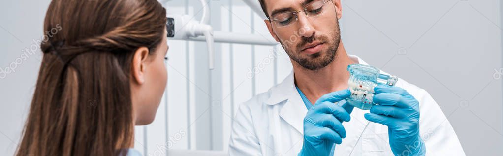 panoramic shot of dentist holding tooth model near woman 