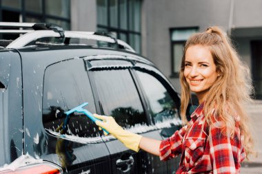 cheerful young woman washing wet car with squeegee  clipart