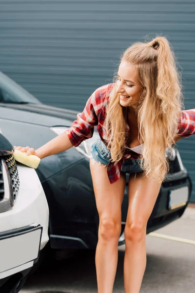 快乐的女人拿着黄色海绵 而洗车 — 图库照片