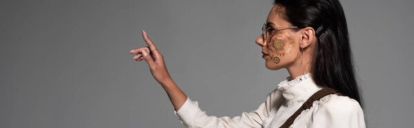 panoramic shot of steampunk woman in glasses looking away and gesturing isolated on grey