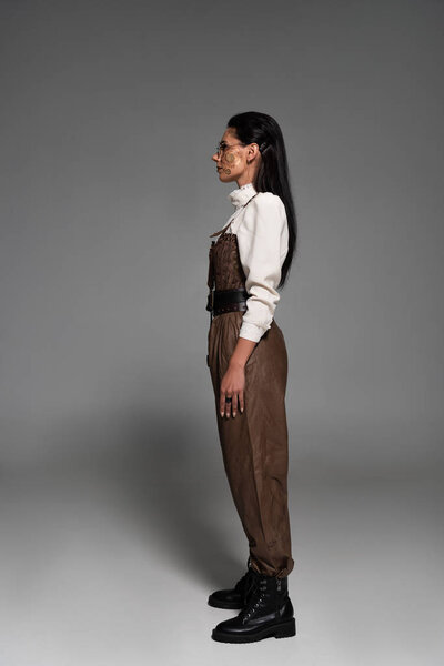 full length view of attractive steampunk woman in glasses on grey