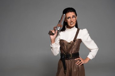 endişeli steampunk kadın kalça el ile ayakta ve gri izole vintage tabanca tutarak