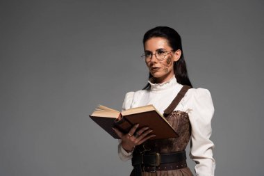 açık kitap tutan gözlük pensive steampunk kadın ve gri izole uzağa bakıyor