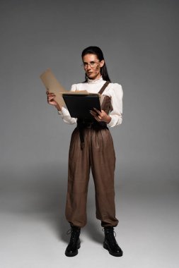 gri üzerinde belgeleri tutan gözlük steampunk kadın tam uzunlukta görünümü