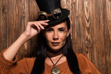 ahşap kamera bakarak gözlük ile üst şapka dokunarak steampunk kadın ön görünümü