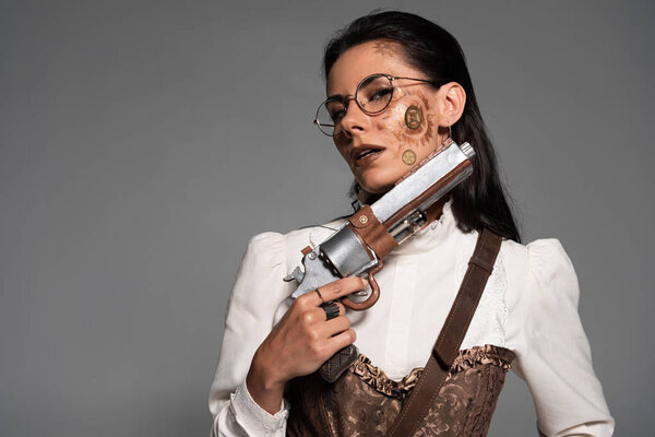 pensive attractive steampunk woman holding vintage pistol isolated on grey