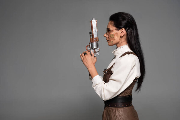 side view of attractive steampunk woman holding vintage pistol isolated on grey