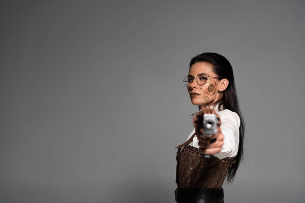selective focus of confident steampunk woman aiming with pistol at camera isolated on grey