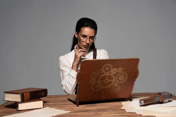 蒸汽朋克妇女在眼镜与文件和老式笔记本电脑在工作场所隔离在灰色 — 图库照片