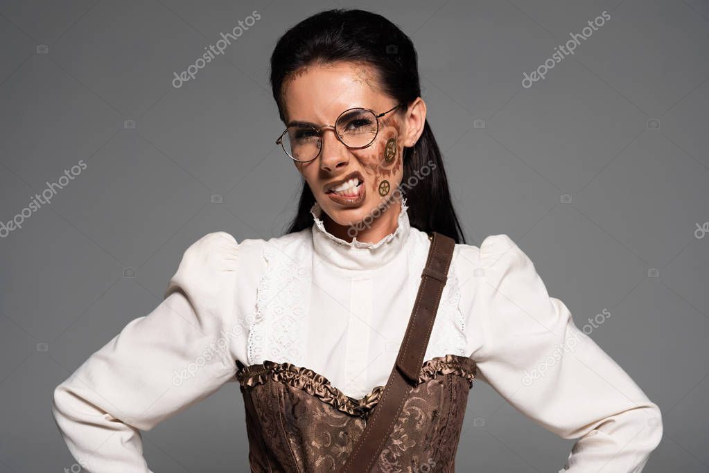 angry steampunk woman in glasses with makeup looking at camera isolated on grey