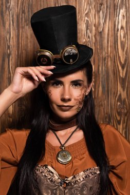 front view of steampunk woman touching top hat with goggles looking at camera on wooden clipart