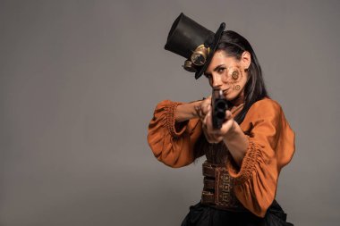 focused steampunk woman in top hat aiming with gun isolated on grey clipart