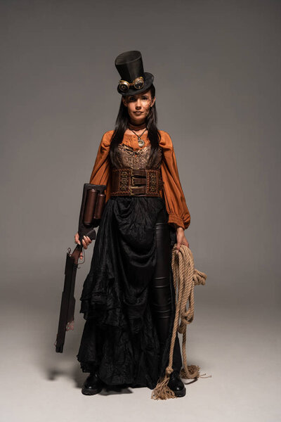 full length view of attractive steampunk woman holding guy and lasso on grey