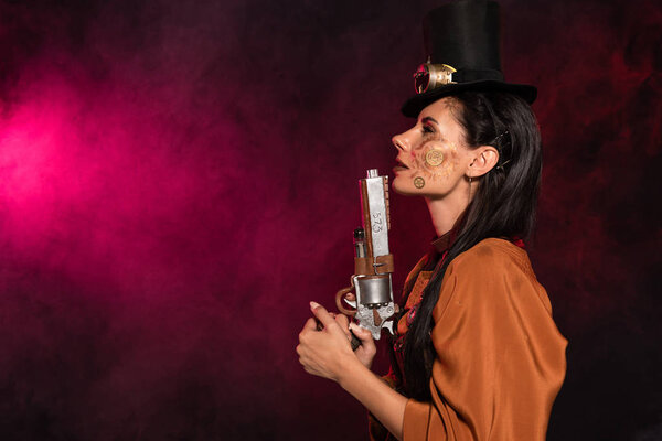 side view of beautiful steampunk woman in top hat holding pistol in pink smoke