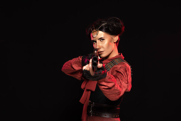 selective focus of steampunk woman aiming with gun to camera isolated on black