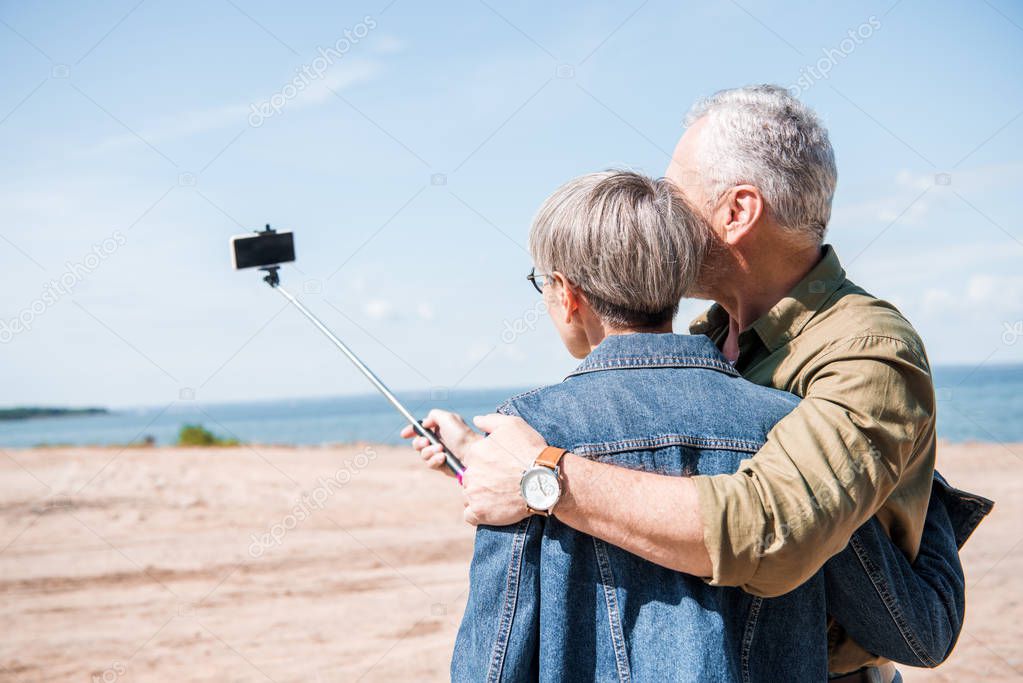 back view of senior couple embracing and taking selfie in sunny day