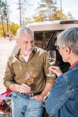 happy senior couple standing near car with wine glasses and looking at each other clipart