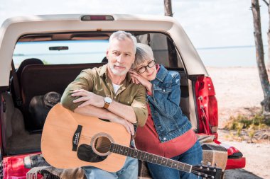 güneşli bir günde araba yakınında akustik gitar ile mutlu yaşlı çift
