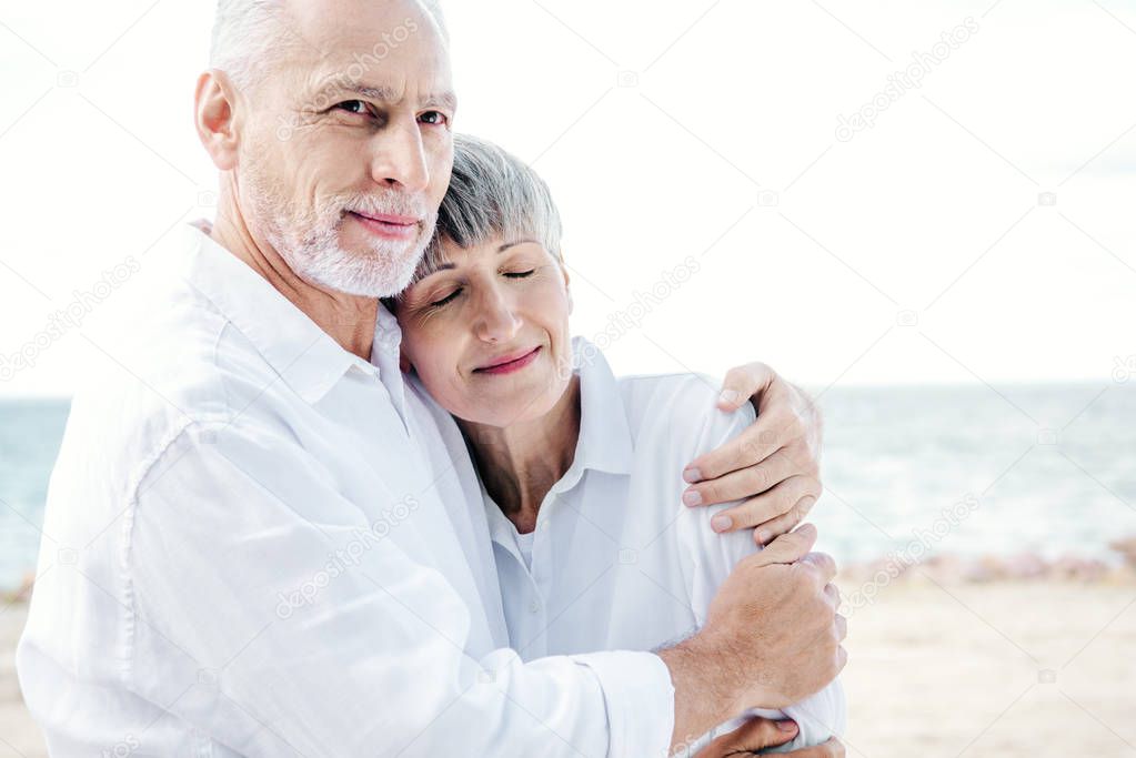 happy senior couple in white shirts embracing at beach