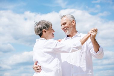 mavi gökyüzü altında dans ederken birbirlerine bakan mutlu yaşlı çift