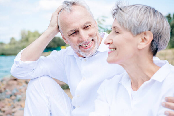 happy smiling senior couple in white shirts embracing under blue sky