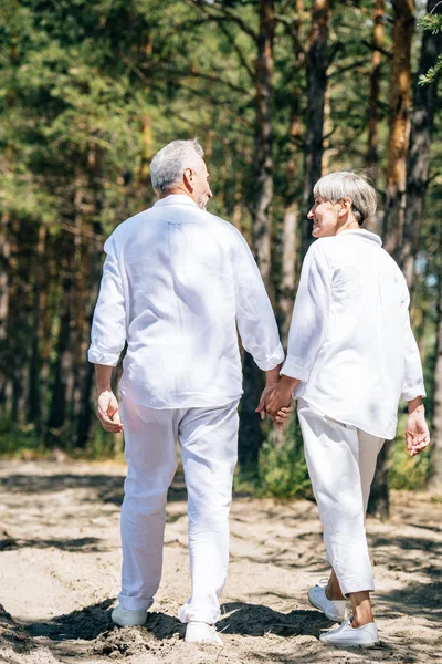 在森林里手牵手 看着彼此的幸福老年夫妇在白色衬衫的背面 — 图库照片