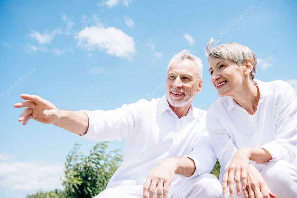 happy smiling senior couple in white shirts looking away under blue sky