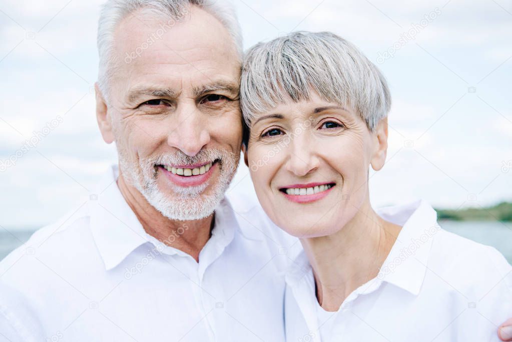 front view of smiling happy senior couple in white shirts looking at camera