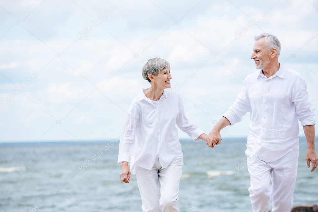 happy senior couple holding hands and looking at each other near river
