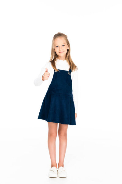 full length view of cheerful schoolgirl looking at camera and showing thumb up on white background