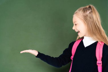 cheerful schoolgirl pointing with hand at green chalk board  clipart