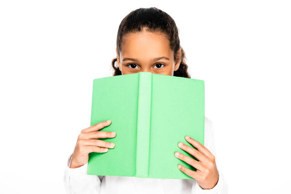 милая африканская американская школьница смотрит в камеру, скрывая лицо книгой, изолированной на белом