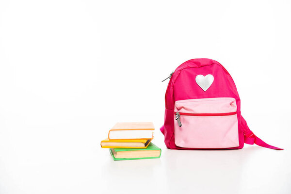 pink backpack with heart symbol and stack of books on white background with copy space