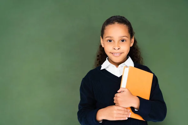 Adorable Afroamericana Colegiala Sosteniendo Libro Mirando Cámara Mientras Está Pie —  Fotos de Stock