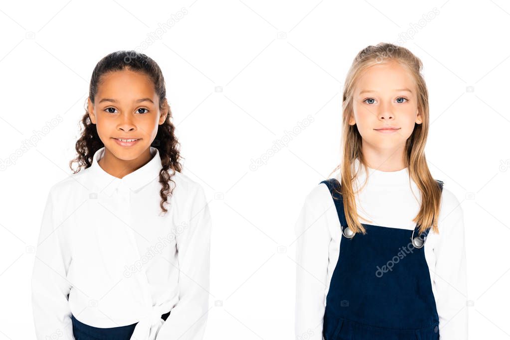 two adorable multicultural schoolgirls smiling at camera isolated on white
