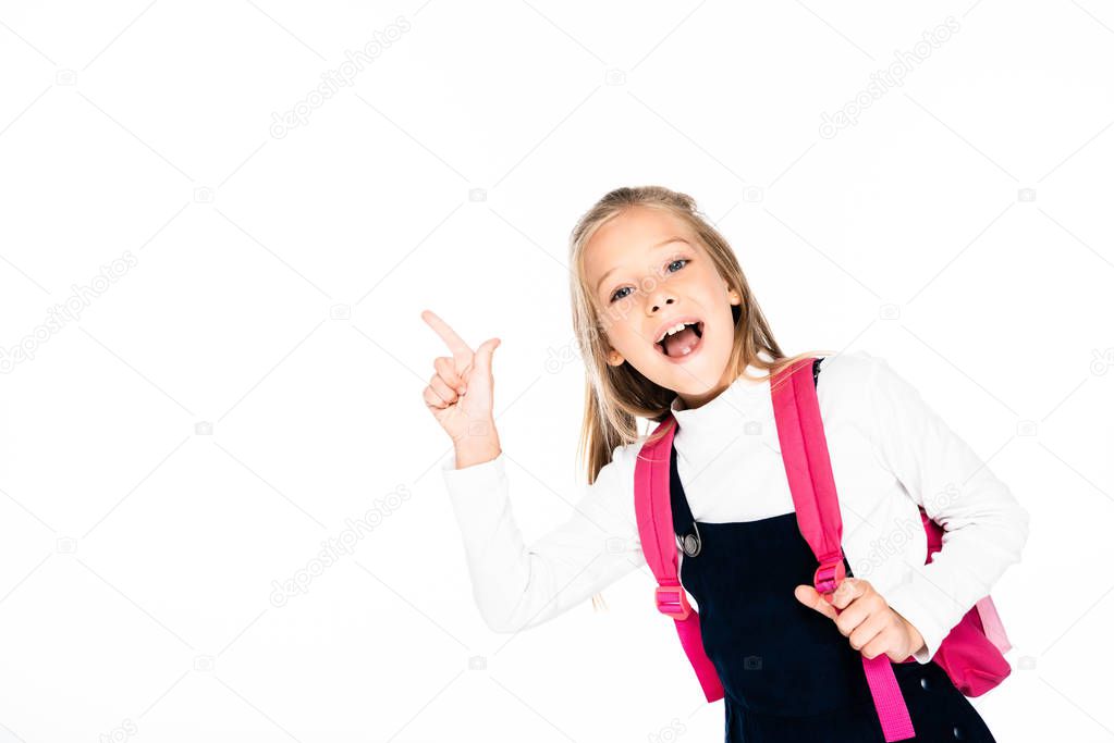 cheerful schoolgirl pointing with finger while smiling at camera isolated on white
