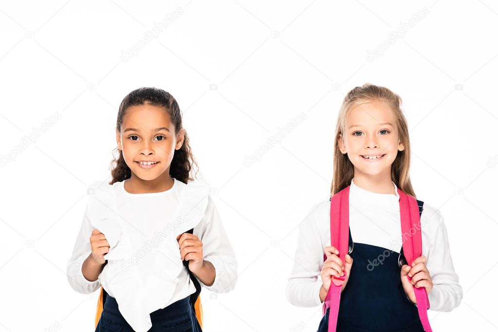 two cute multicultural schoolgirls smiling at camera isolated on white